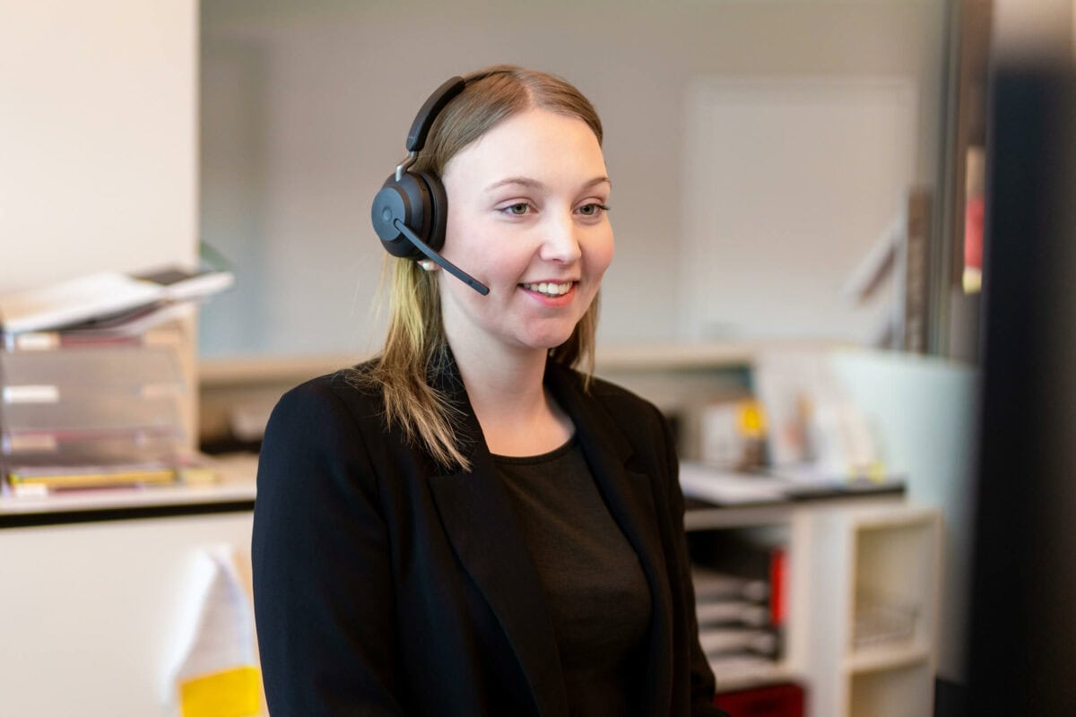Mitarbeiterin mit Headset lächelt im Kundengespräch an ihrem Arbeitsplatz