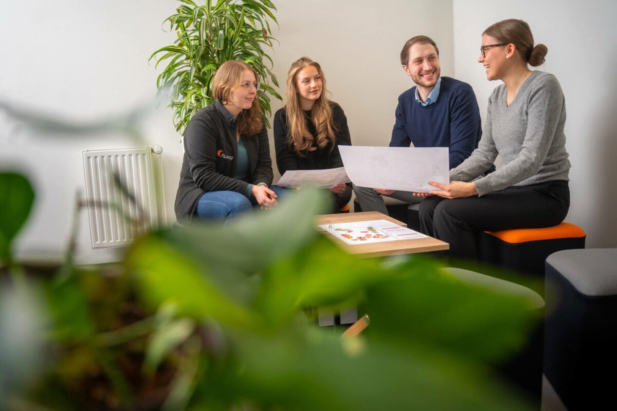 Vier Mitarbeitende einer Wohnungsbaugesellschaft besprechen einen Grundriss auf Sitzwürfeln im Büro