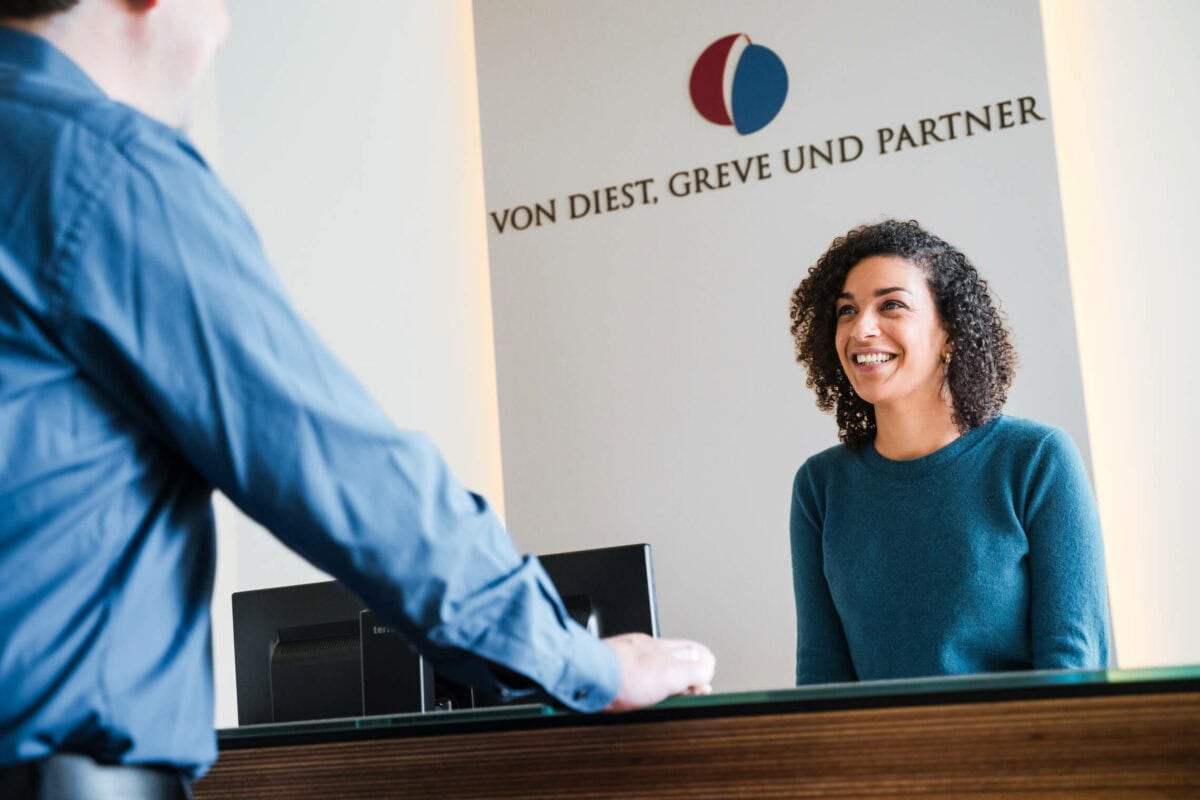 Mitarbeiterin am Empfang von von Diest, Greve und Partner begrüßt lächelnd einen Besucher